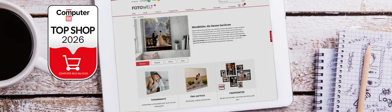 Auszeichnung als Top Shop 2026 für ROSSMANN Fotowelt Unsere Website auf einem Tablet mit der Top Shop 2026 Auszeichnung von Computer Bild, daneben eine Tasse Kaffee und Notizbücher.