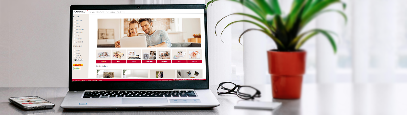 kostenlose ROSSMANN Fotowelt Software, App und Online-Editor Ein Laptop auf einem Tisch mit der geöffneten ROSSMANN Fotowelt Software, daneben eine Brille, eine Pflanze und ein Handy mit der Fotowelt App.