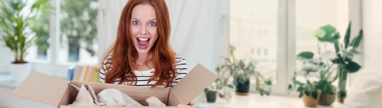 Fotogeschenke Ideen: Unsere Neuheiten Frau macht ein überraschtes Gesicht, als sie im Karton die ROSSMANN Neuheiten entdeckt. Jetzt stöbern und inspirieren lassen!