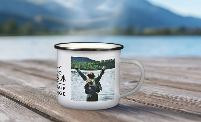 Reisetassen gestalten – Emailletasse mit Urlaubsfoto personalisieren Weiße Emailletasse mit Foto und dekorativem Design, platziert auf einem Holzsteg