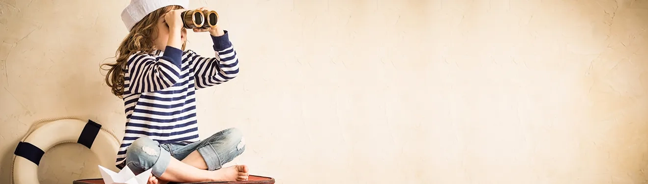 Angebot des nächsten Monats entdecken Ein Kind im Matrosenlook sitzt auf einem Koffer und hält mit einem Fernglas Ausschau nach dem Angebot des nächsten Monats.