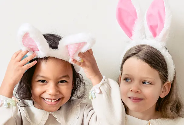 Foto-Geschenkideen: ROSSMANN Osterwelt Zwei Kinder mit Hasenohren-Stirnbändern lachen fröhlich. Entdeckt unsere Fotogeschenke-Ideen zu Ostern für die ganze Familie!