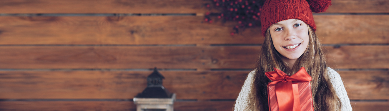 Fotogeschenke für Weihnachten entdecken Kind mit roter Mütze hält ein verpacktes personalisiertes Weihnachtsgeschenk mit großer roter Schleife in den Händen.