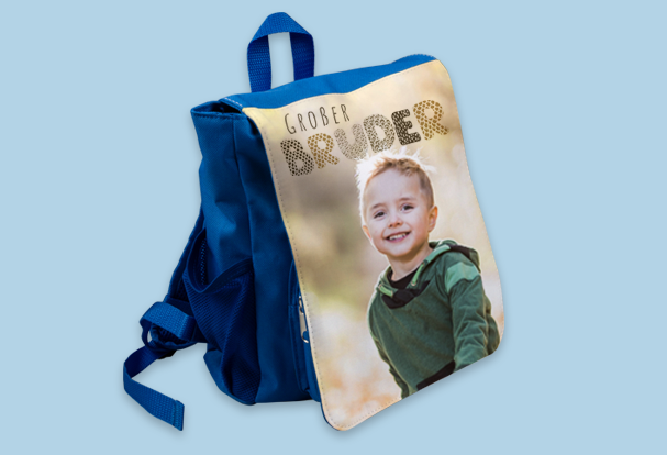 Kinderrucksack als Babygeschenk zur Geburt gestalten Ein blauer Kinderrucksack mit individuell bedruckter Vorderseite, die ein fröhliches Kind und den Text „Großer Bruder“ zeigt – ein kreatives und praktisches Babygeschenk zur Geburt
