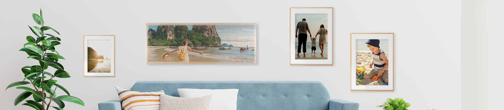 Individuell gestaltete Wanddekoration bringen ein Stück Urlaub mit nach Hause Wohnzimmerszene mit unterschiedlichen Wandbildern, über blauer Couch großes Foto auf Holz, links und rechts daneben gerahmte Poster, Mehrteilige Leinwand auf der rechten Seite mit Strandmotiv