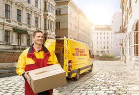 Hier Antworten auf allgemeine Fragen, wie Lieferzeit, erhalten DHL-Lieferfahrer in uniformiertem Gelb-Rot-Outfit trägt Paket aus einem geöffneten Lieferwagen in städtischer Umgebung.