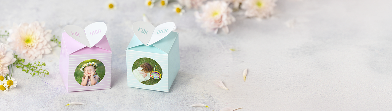 Fotos im Geschenkkuvert liebevoll verpacken Ein quadratisches Familienfoto und ein Geschenkkuvert mit Herzform und Foto auf hellem Untergrund, umrahmt von Blumen