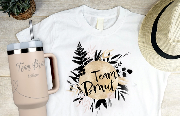 T-Shirts und Thermobecher zur Hochzeitsplanung Weißes T-Shirt mit Desing und Schriftzug 'Team Braut', daneben Thermobecher mit Text 'Team Braut Kathleen' als stylishe Fotogeschenke Hochzeit.
