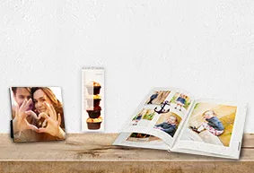 Antworten auf Fragen zum Bilderdienst erhalten Verschiedene personalisierte Fotoprodukte wie ein Fotoaufsteller, ein Terminkalender und ein Fotobuch auf einem Holztisch.